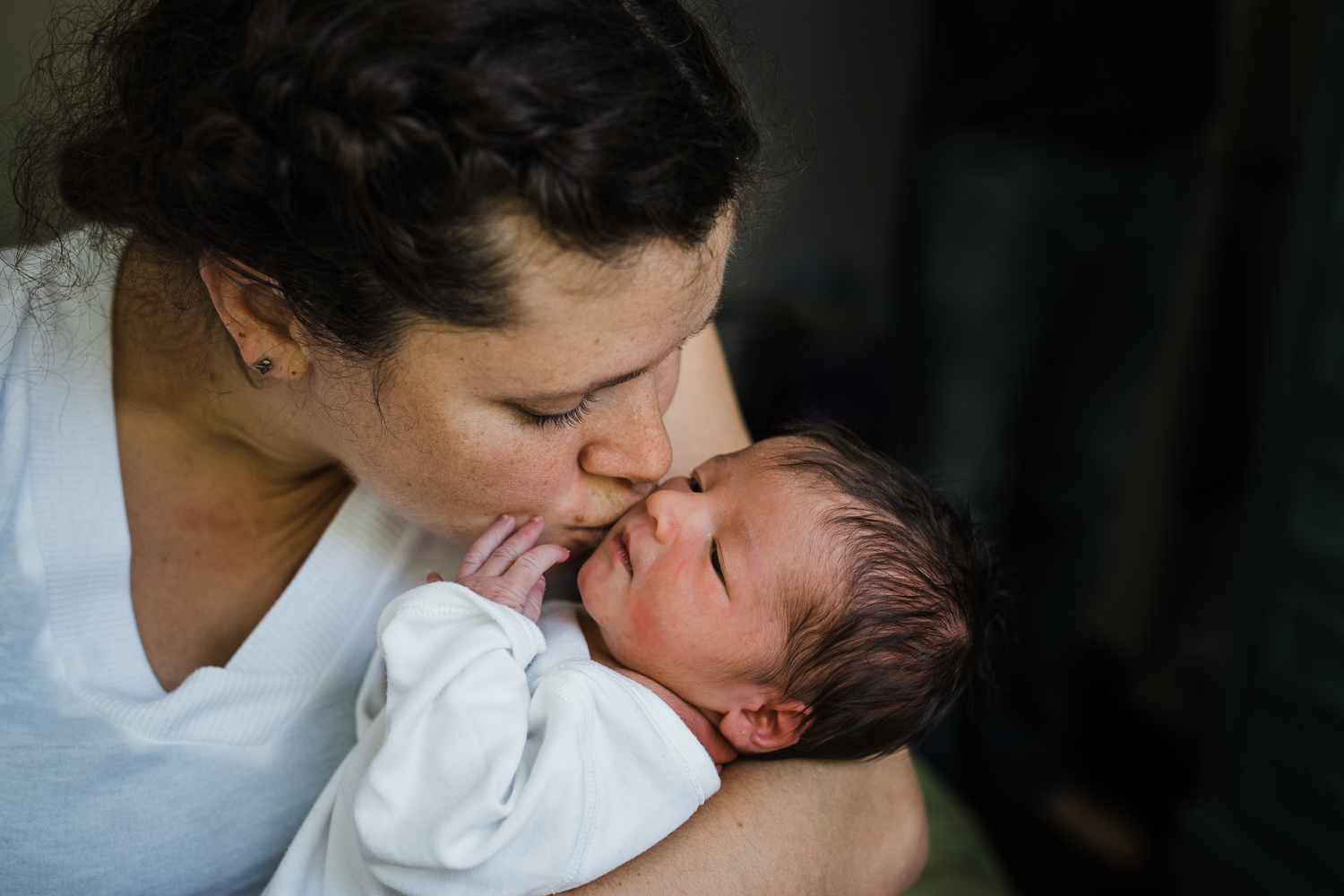 A mom holding her two day old baby close in her arms and kissing his cheeks at home during photo session.