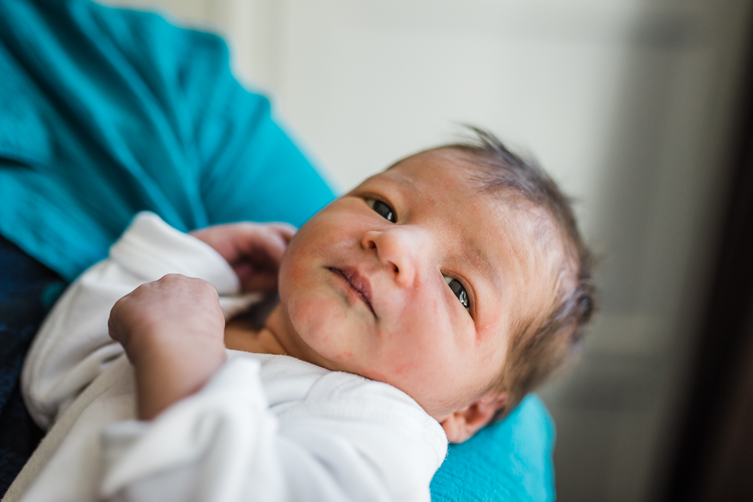 A portrait of a two day old newborn held in Dad's arms with his eyes open.