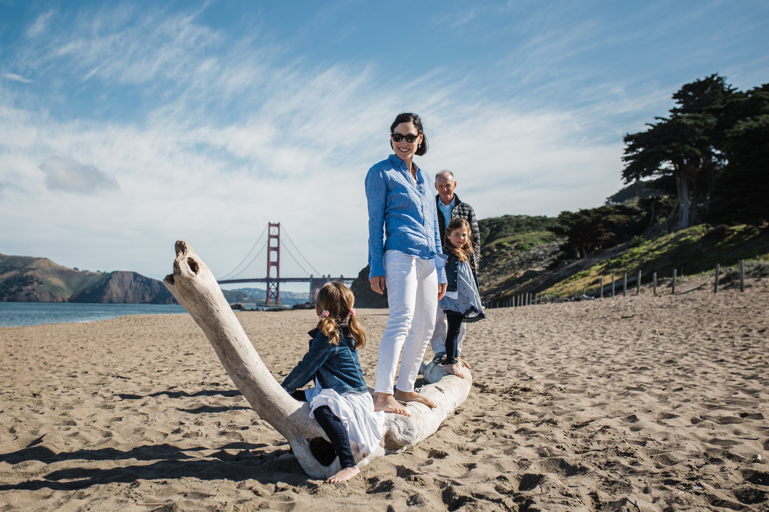 A family of 4 standing on driftwood at Baker Beach beach in San Francisco during family portraits