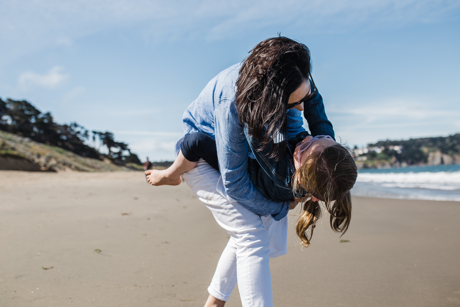 mom holding 5 year old daughter and dipping her down while at Baker beach {SF Family Photographer}