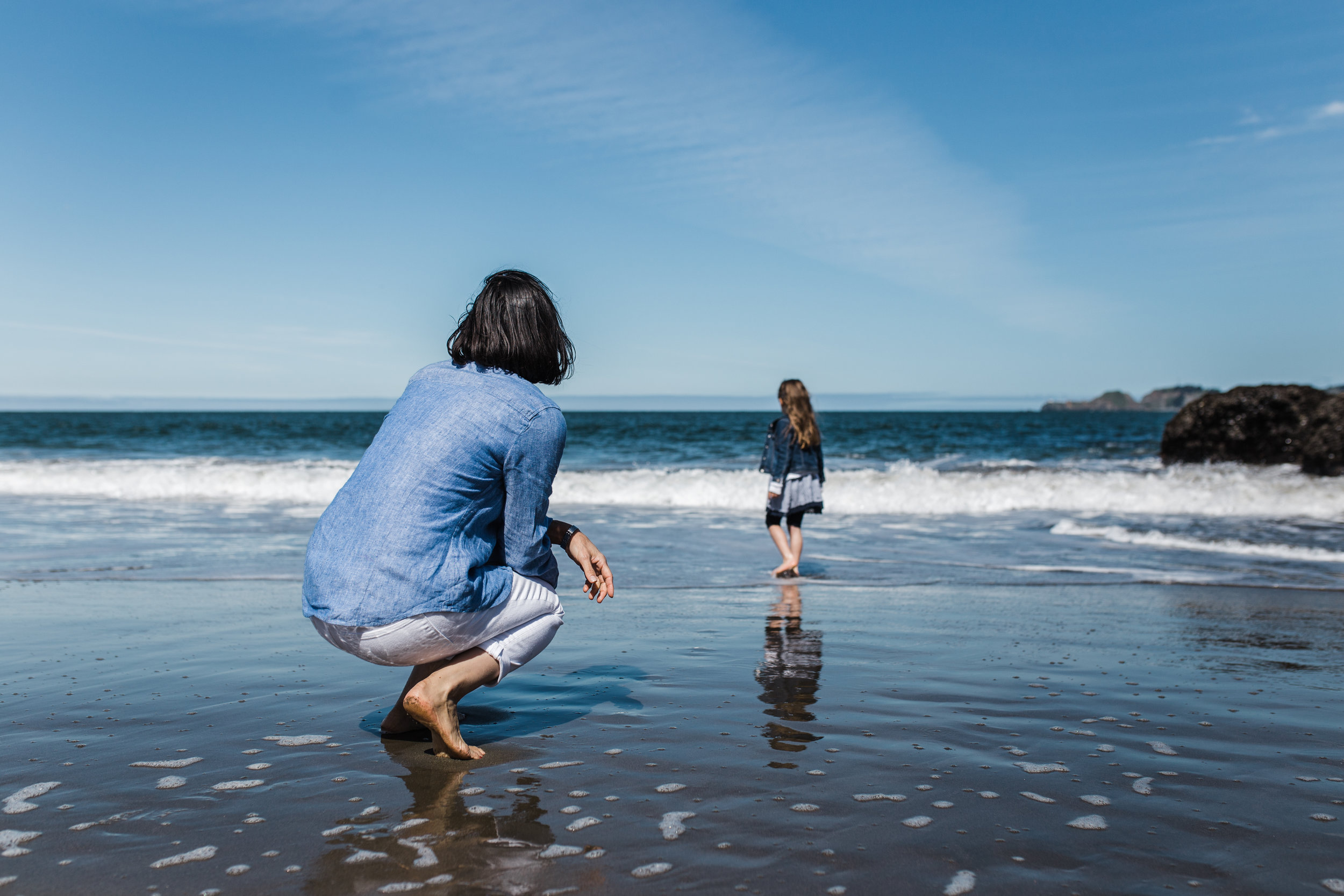 Mom squatting down on the beach watching her five year old daughter wade in the water at Baker Beach {Bay Area Family Photographer}