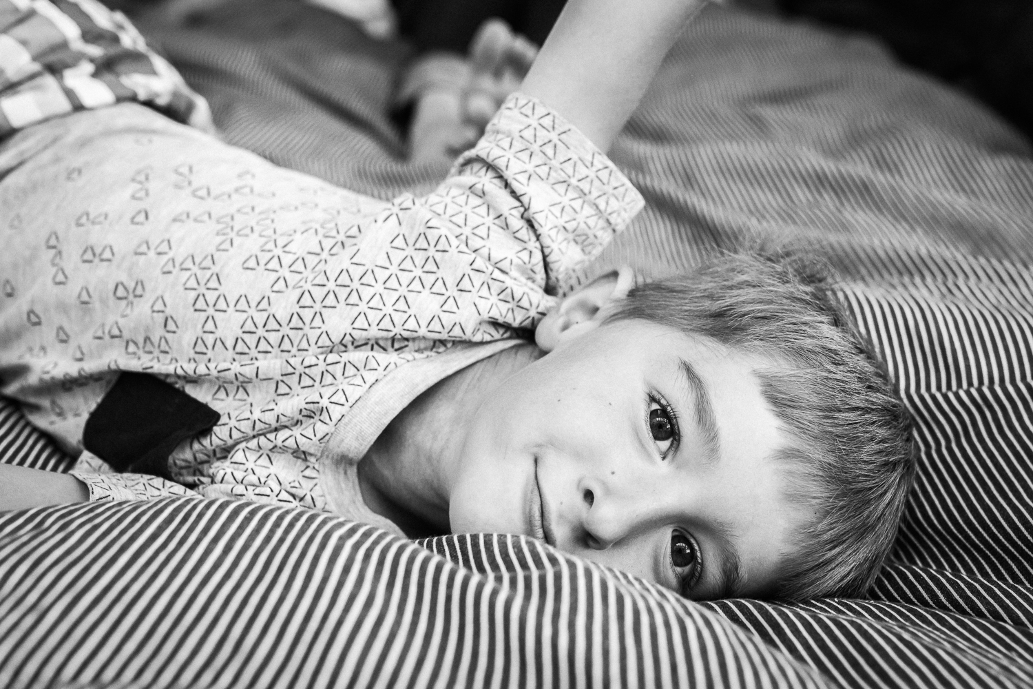  five year old boy laying on his parent’s bed and smiling at the camera