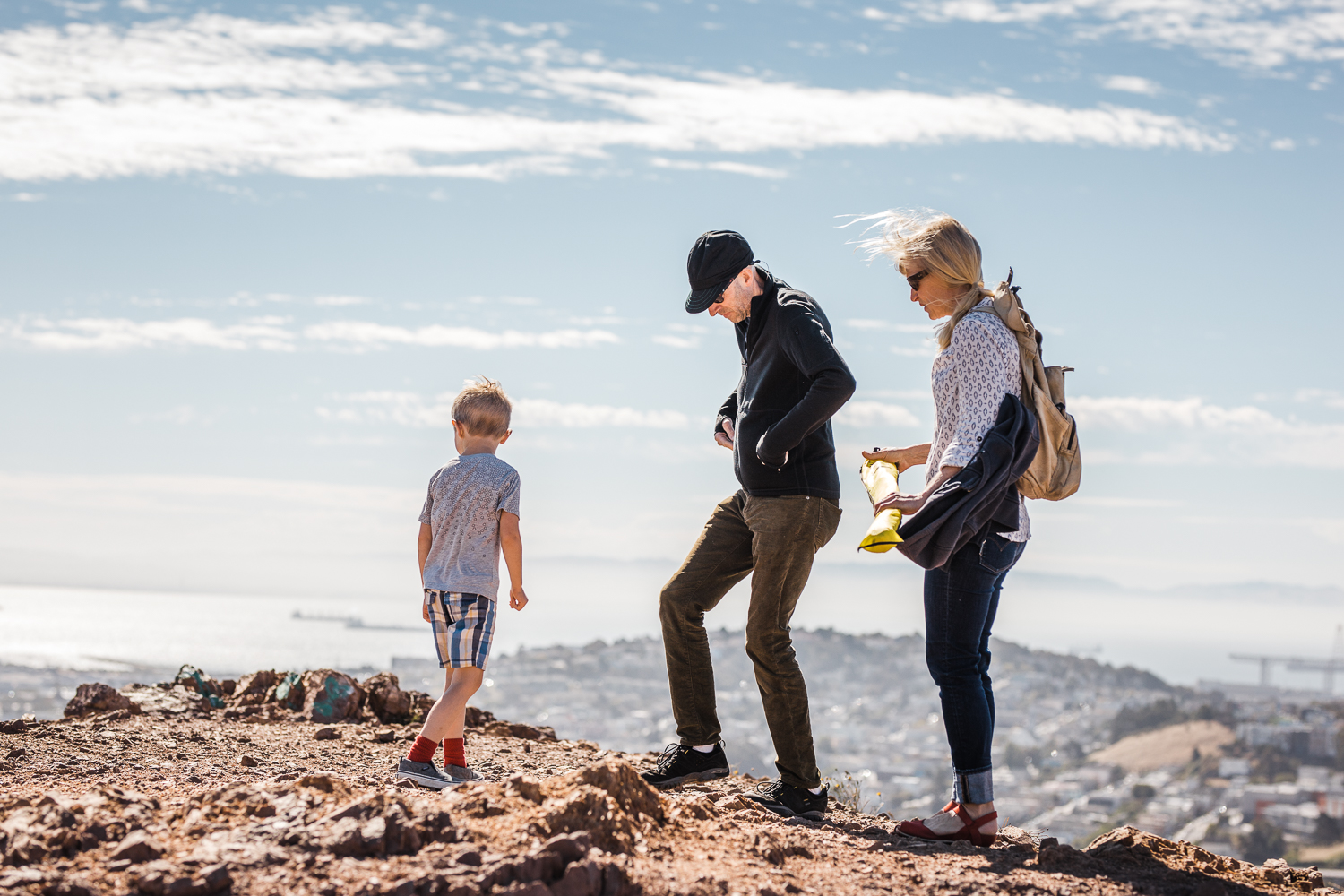 Family of three up on Bernal Hill overlooking San Francisco looking at the view during family session 