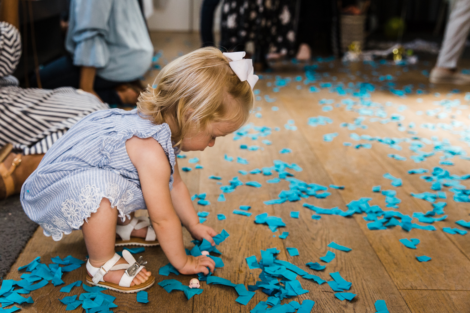 A two year old girl playing with blue confetti on the floor after a gender reveal party 