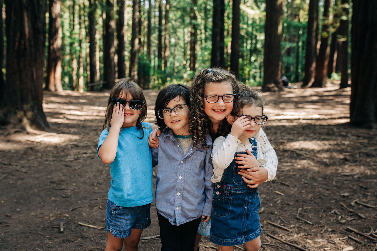 four Cousins all looking at the camera and being silly by wearing their parents’ glasses in the woods in Oakland