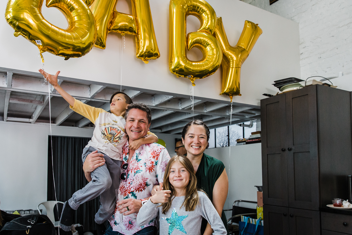 Pregnant aunt and uncle standing with niece and nephew in front of balloons that spell BABY