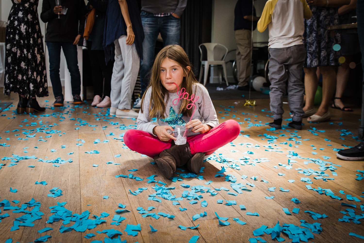 A girl sitting on the floor in the middle of blue confetti after a gender reveal party 