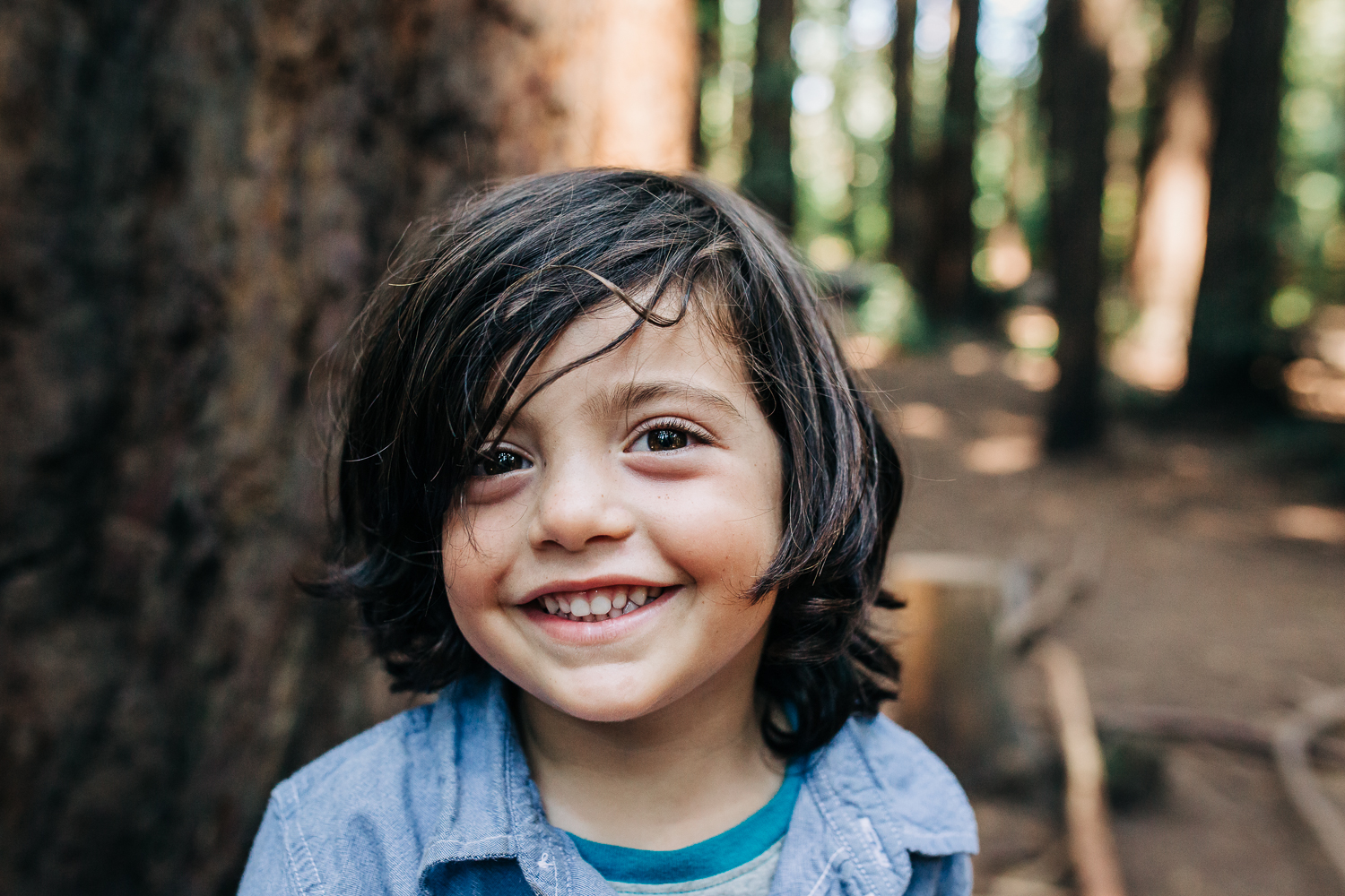 Portrait of a four year old boy looking at the camera and smiling while playing in the woods in Oakland