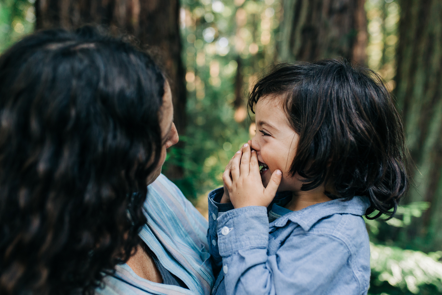 Mom holding four year old son as he looks at her and smiles while in the woods 