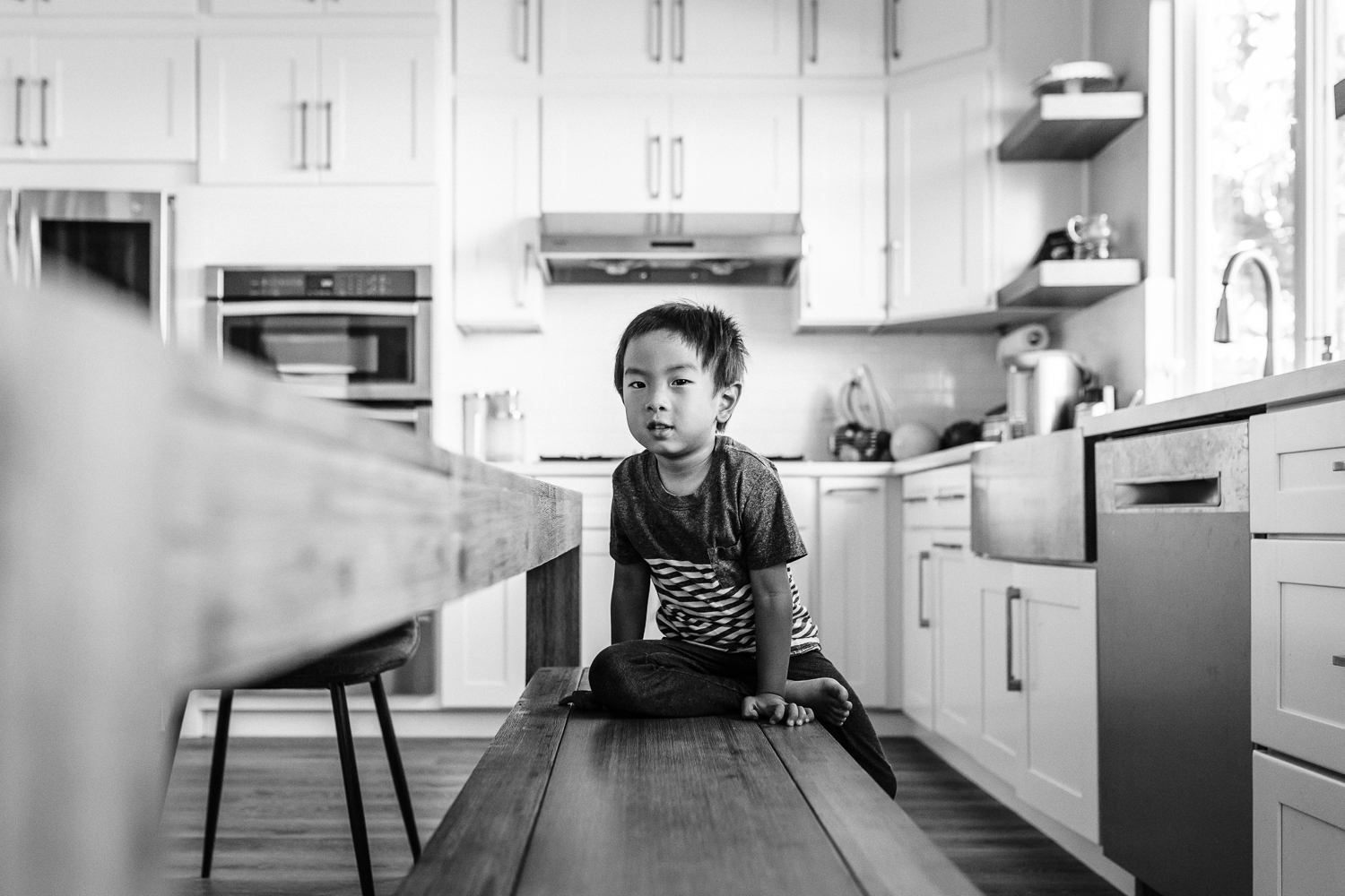 four year old boy sitting on a bench in the kitchen looking at the camera | East Bay Lifestyle Family Photographer