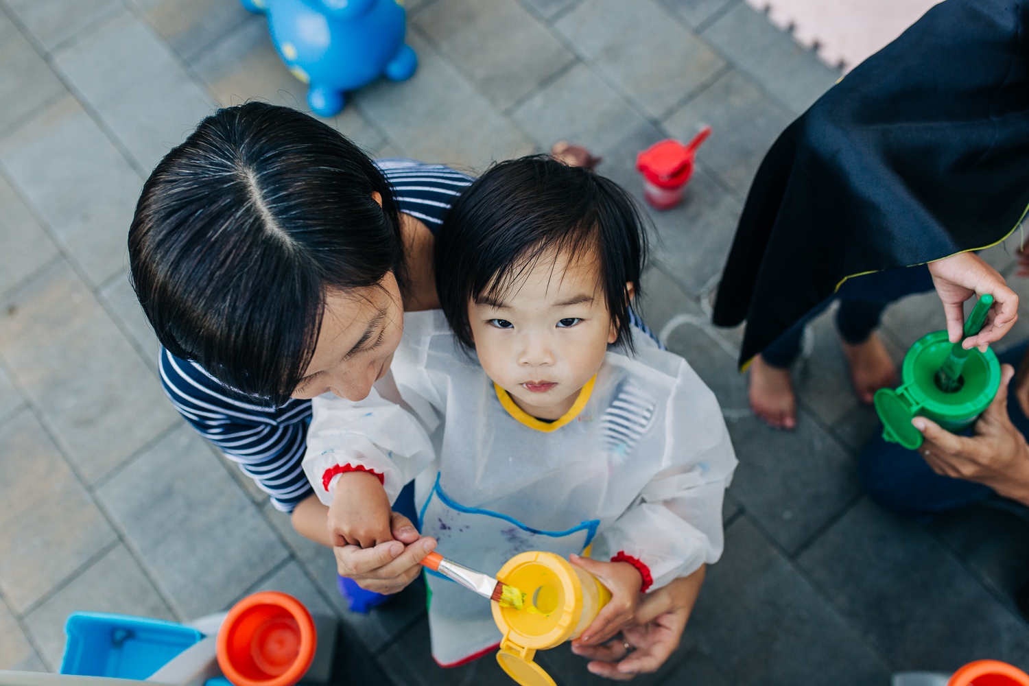 birds eye view of a two year old girl looking up while painting at an easel with her mother