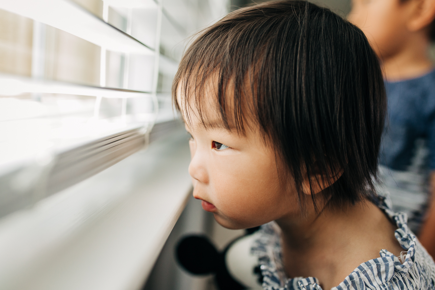 2 year old girl looking out blinds in a window 