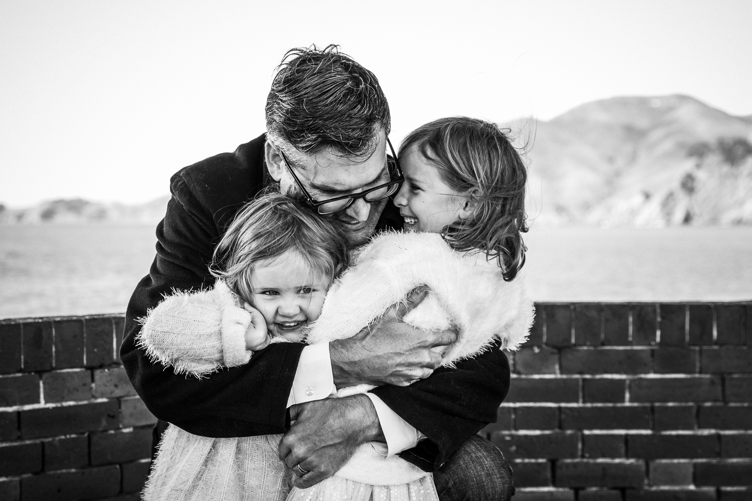 dad hugging his two young girls while they smile 