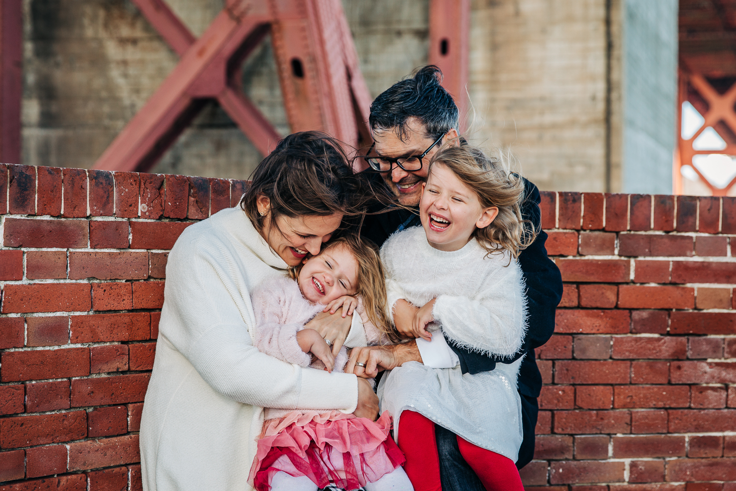 Family of four snuggling in close and laughing on a windy day in San Francisco