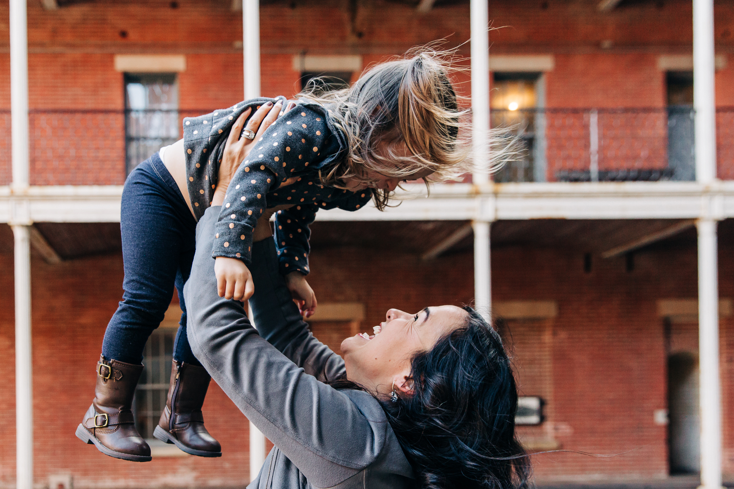 Mother holding up her two year old girl and they are looking into each other's eyes and smiling {