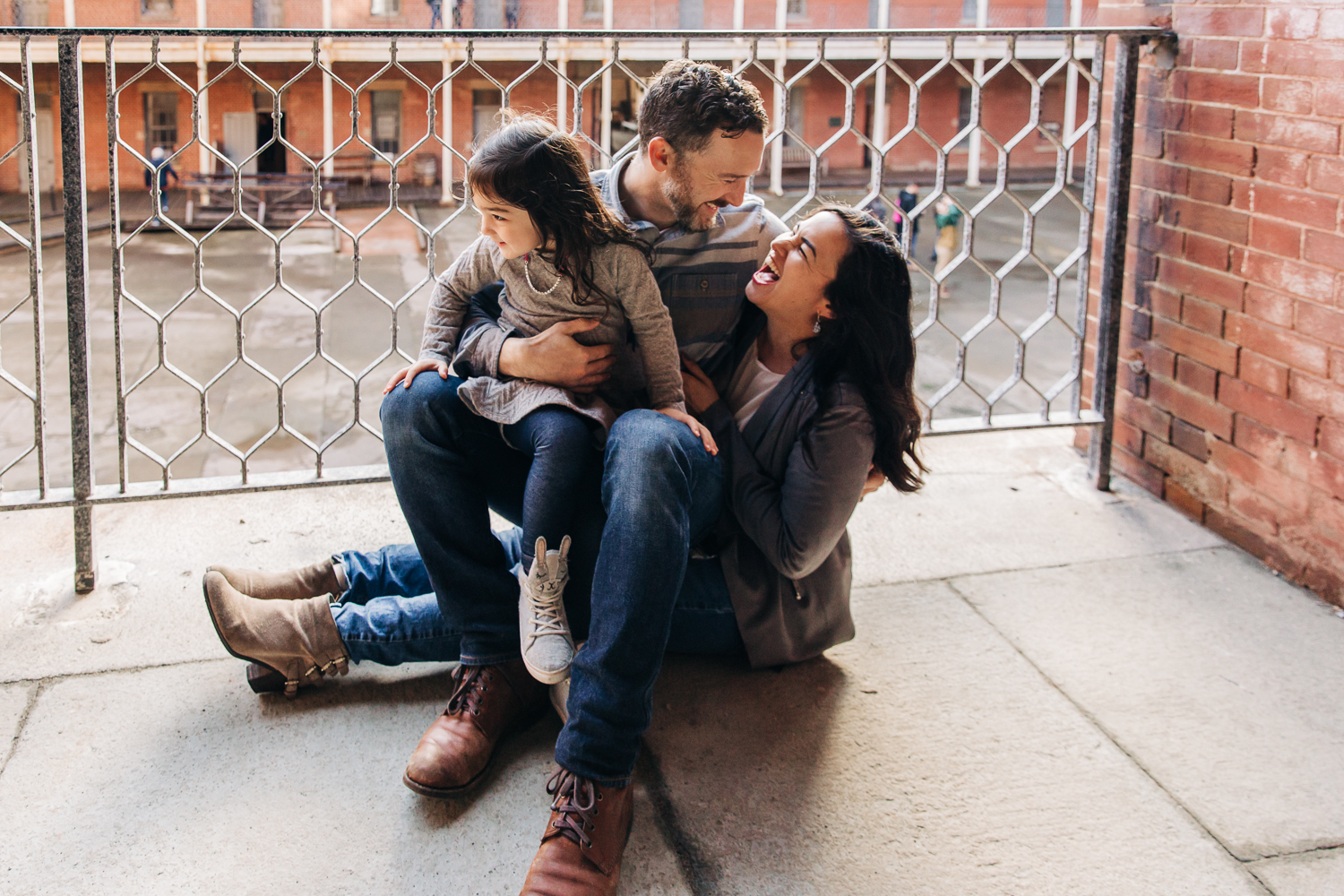 Family sitting on the ground together at Fort Point with mom and dad looking at each other and laughing 