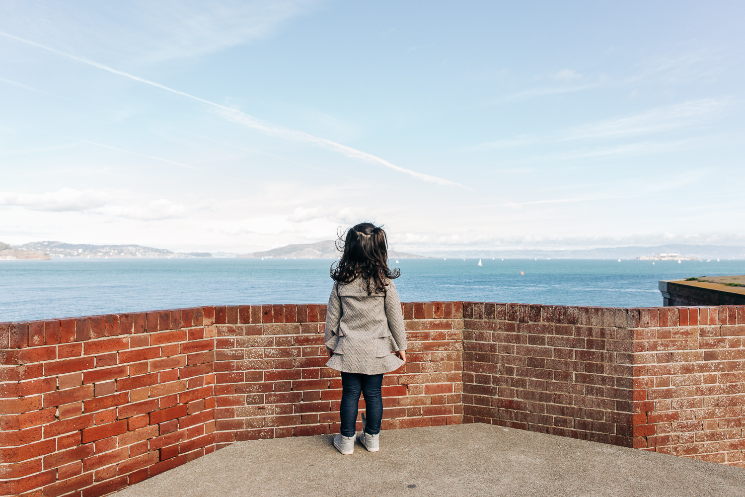 little girl standing at a brick wall and looking out at the San Francisco bay 