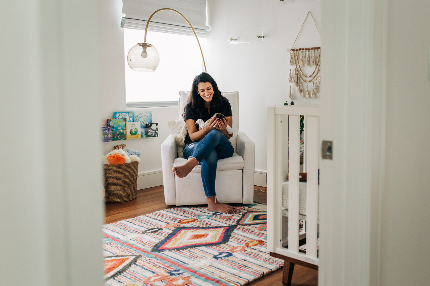 Mother sitting in a rocking chair holding her newborn baby boy in her lap and smiling down at him | SF Baby Photography