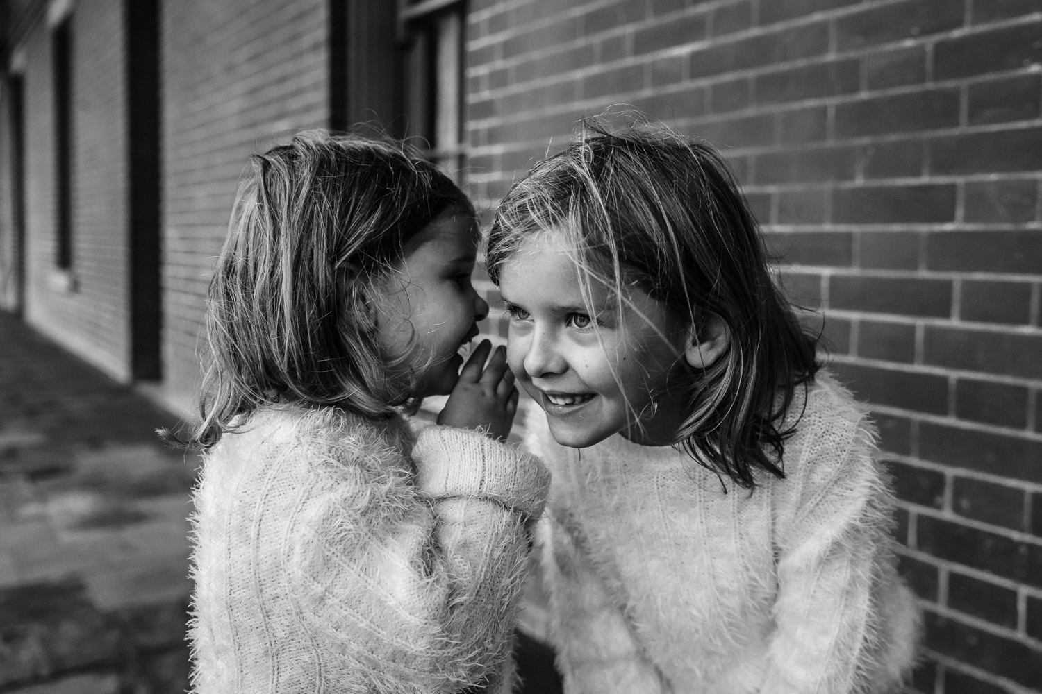 two sisters smiling and telling secrets with each other 