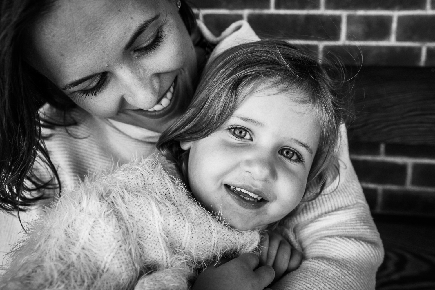 a mom looking down and smiling at her two year old daughter who is looking at the camera 