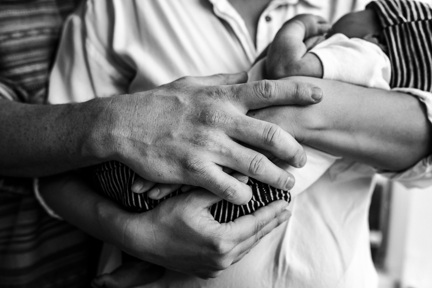 black and white photo of mom and dad holding hands and their newborn baby boy 