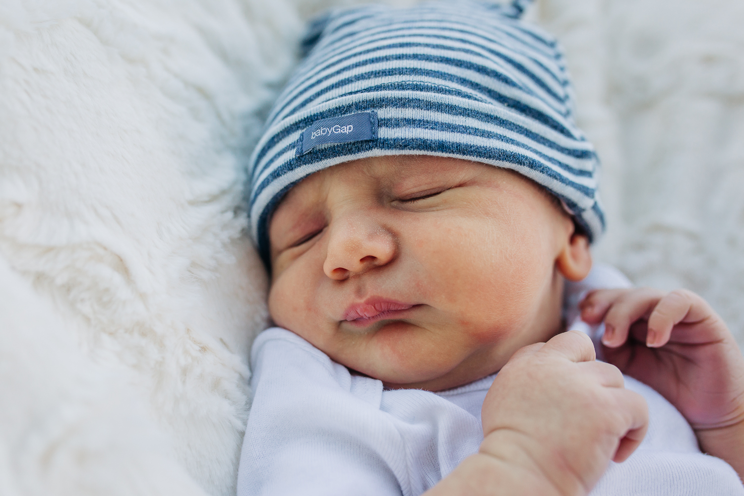 Close up of a newborn boy as he sleeps in a striped blue hat 