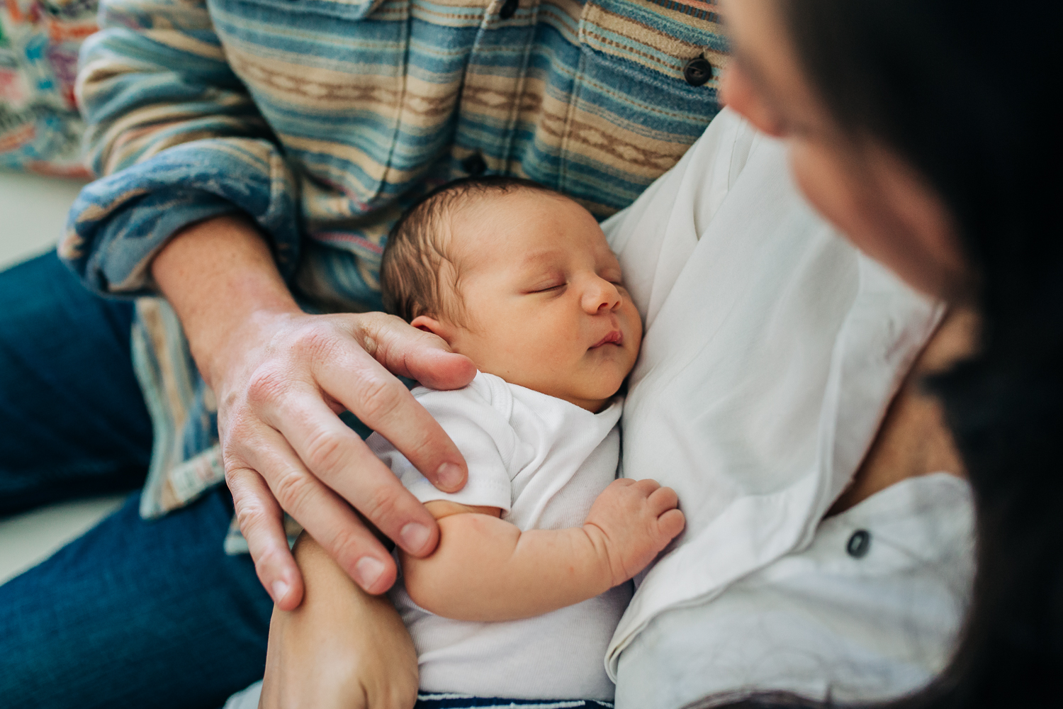 Mother holding baby boy with Dad's hand resting on his shoulder while he sleeps 