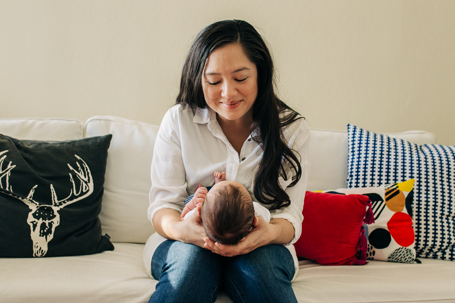 New Mother holding her new baby boy on her lap as she looks down at him smiling 