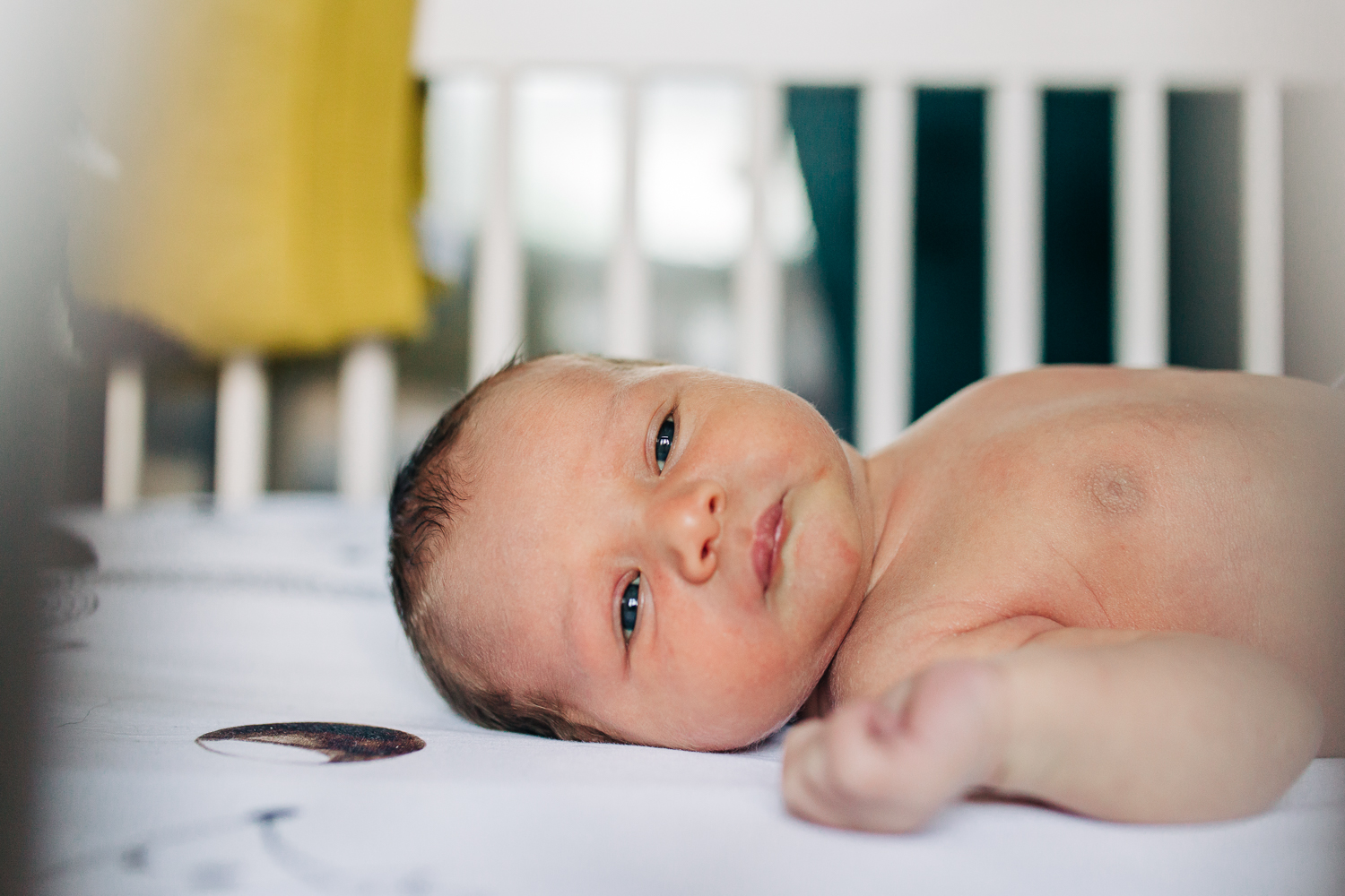 close up of baby boy laying in his crib and looking towards the camera 