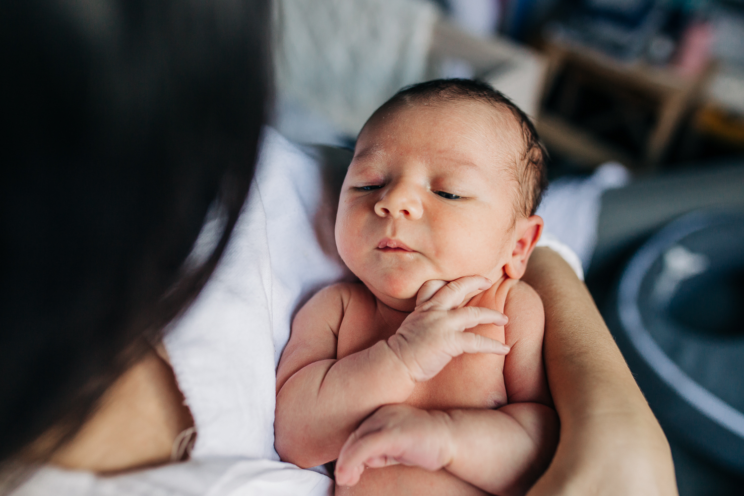 close up of a one week old boy sleeping in his Mom's arms with no clothes on 