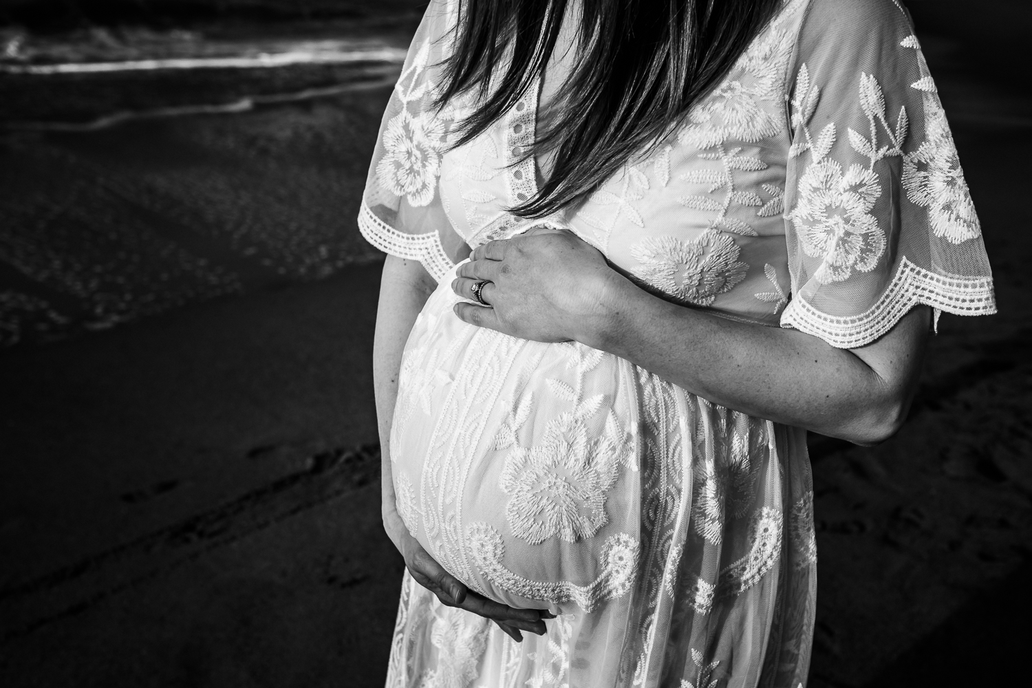 pregnant women wearing long white dress holding baby bump on beach