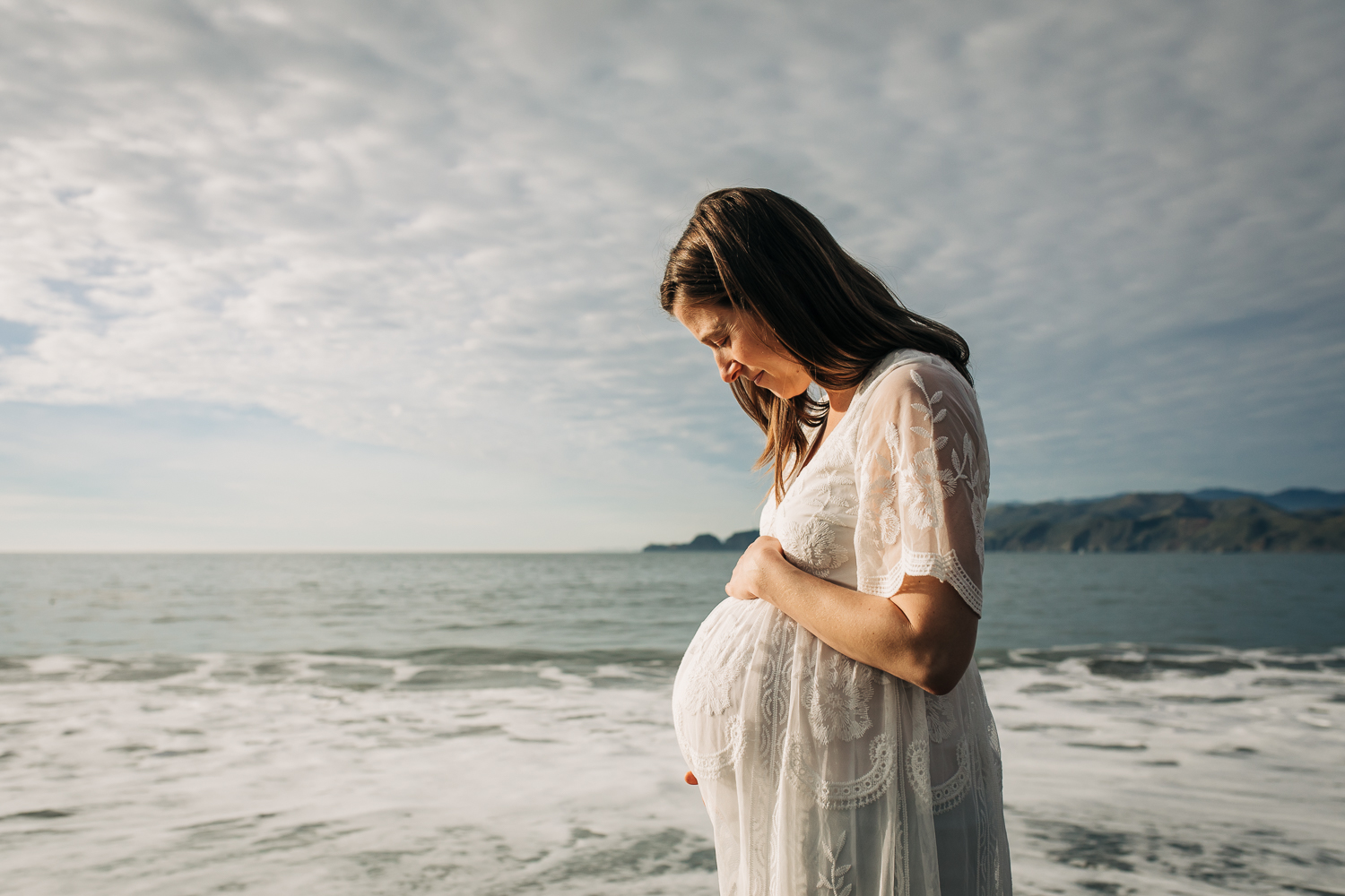 Pregnant mom looking down at her baby bump with the ocean in the background 