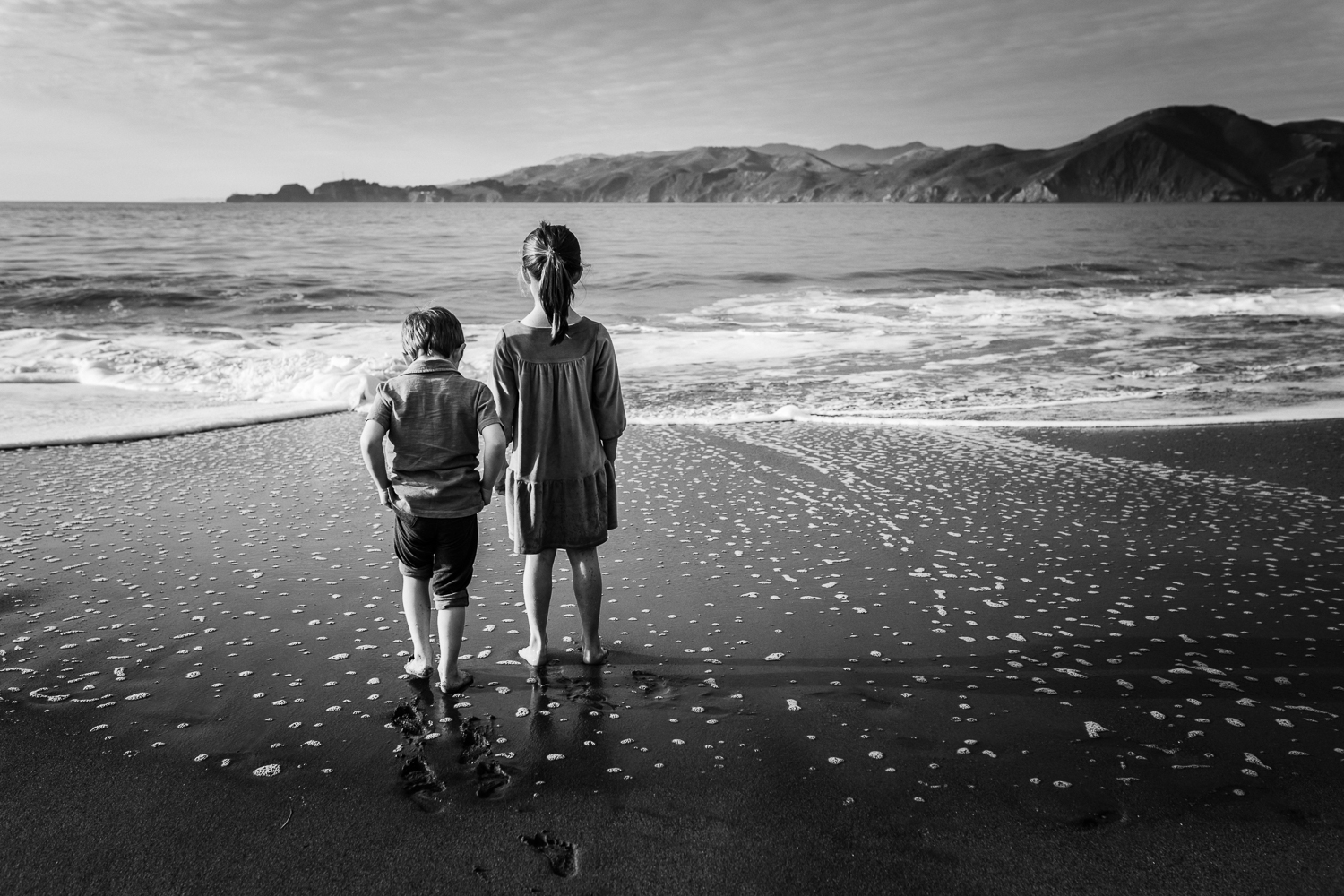 two small children looking out at the ocean while standing on a San Francisco beach