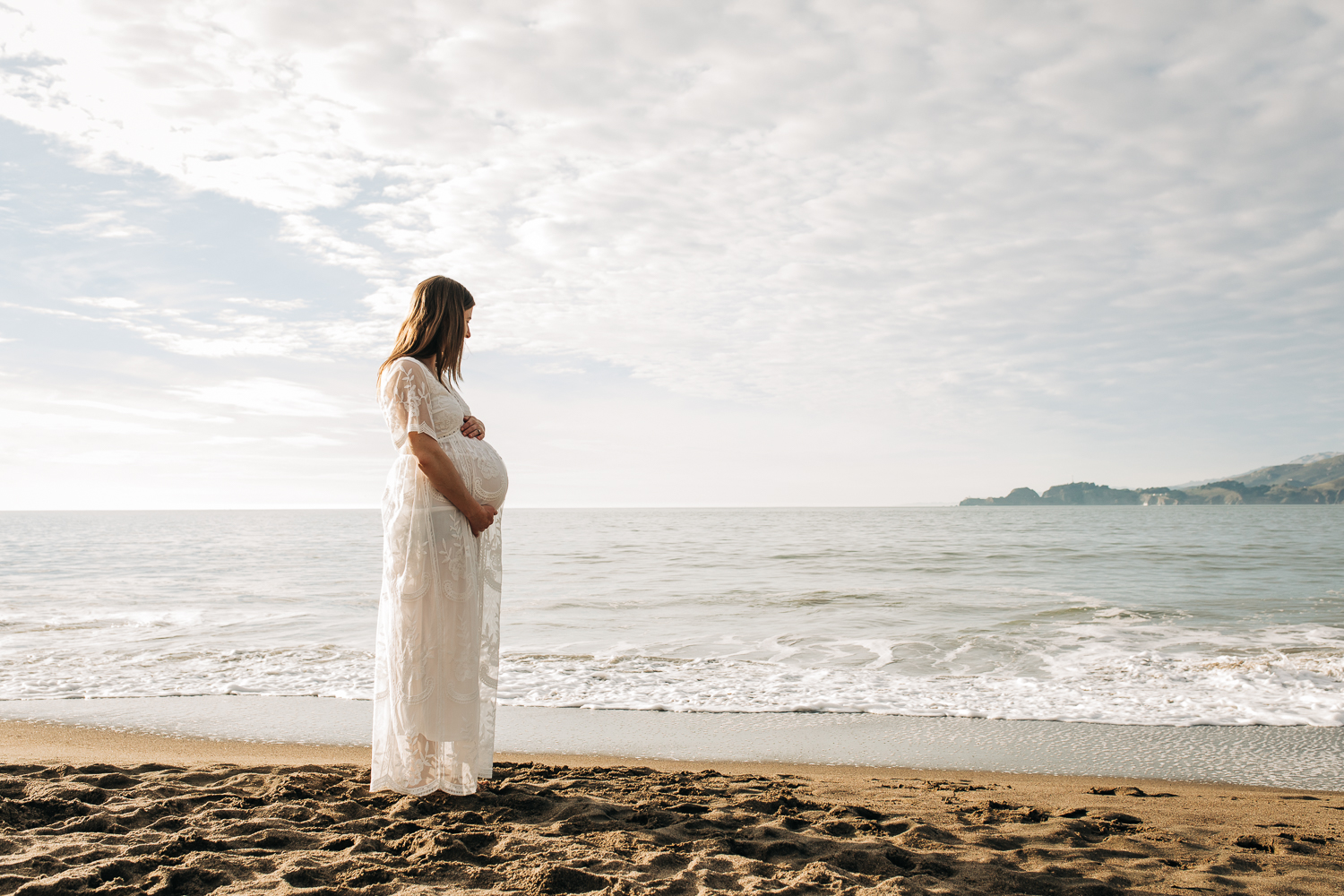 pregnant mother standing on Bay Area beach and looking out at the ocean