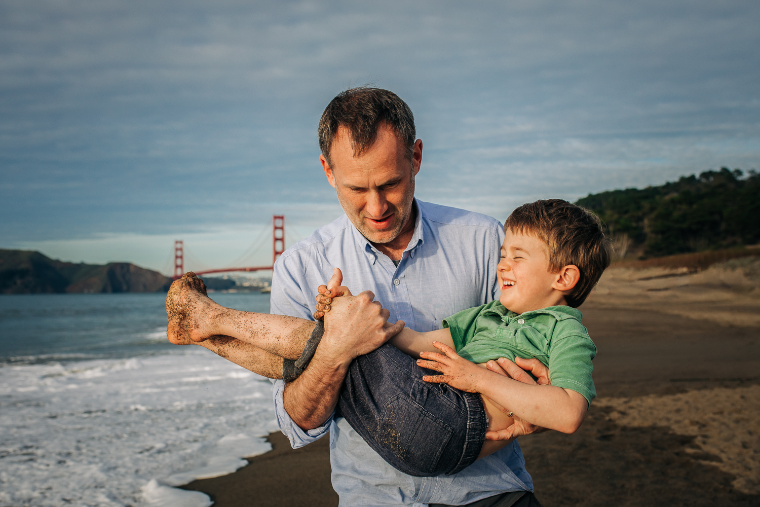 Dad holding his toddler son on the beach while they are both smiling