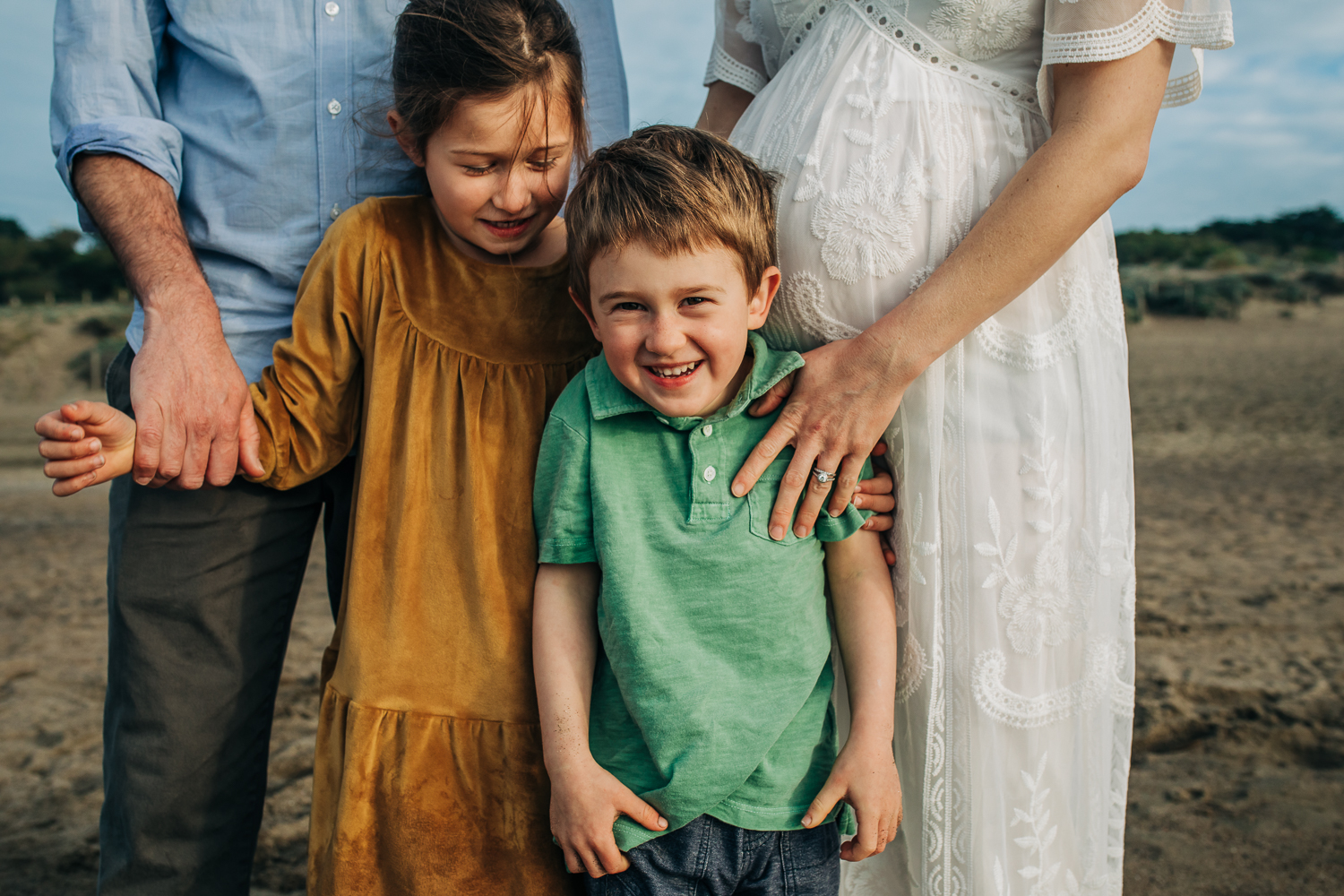 mom and dad and siblings laughing while standing next to their mom's baby bump