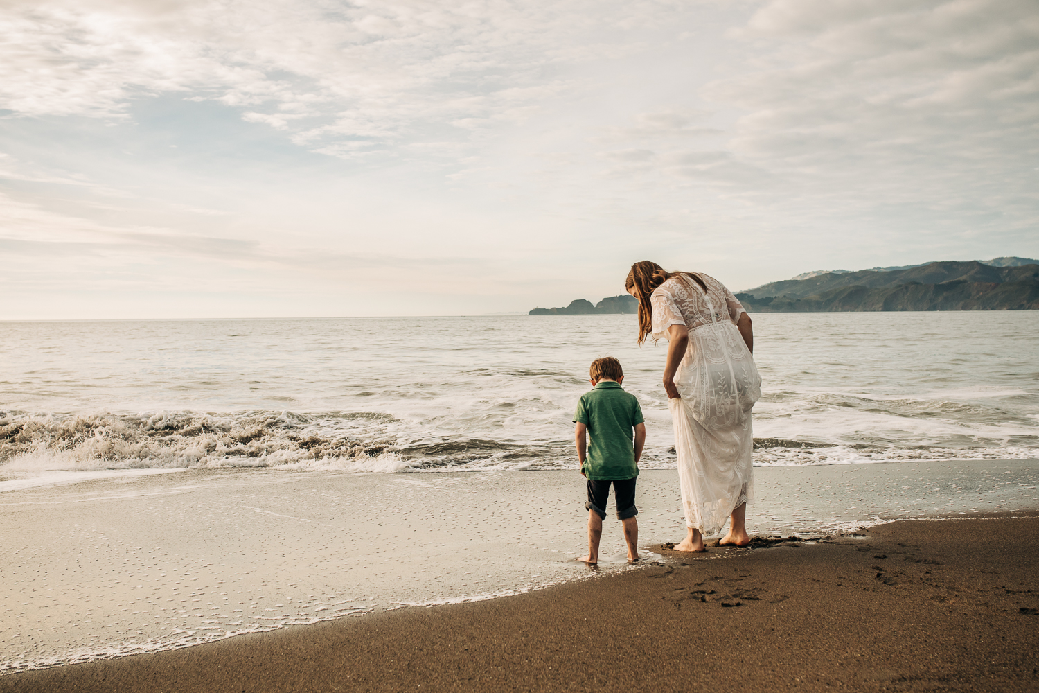 pregnant mother wading in the ocean at the beach with her toddler son