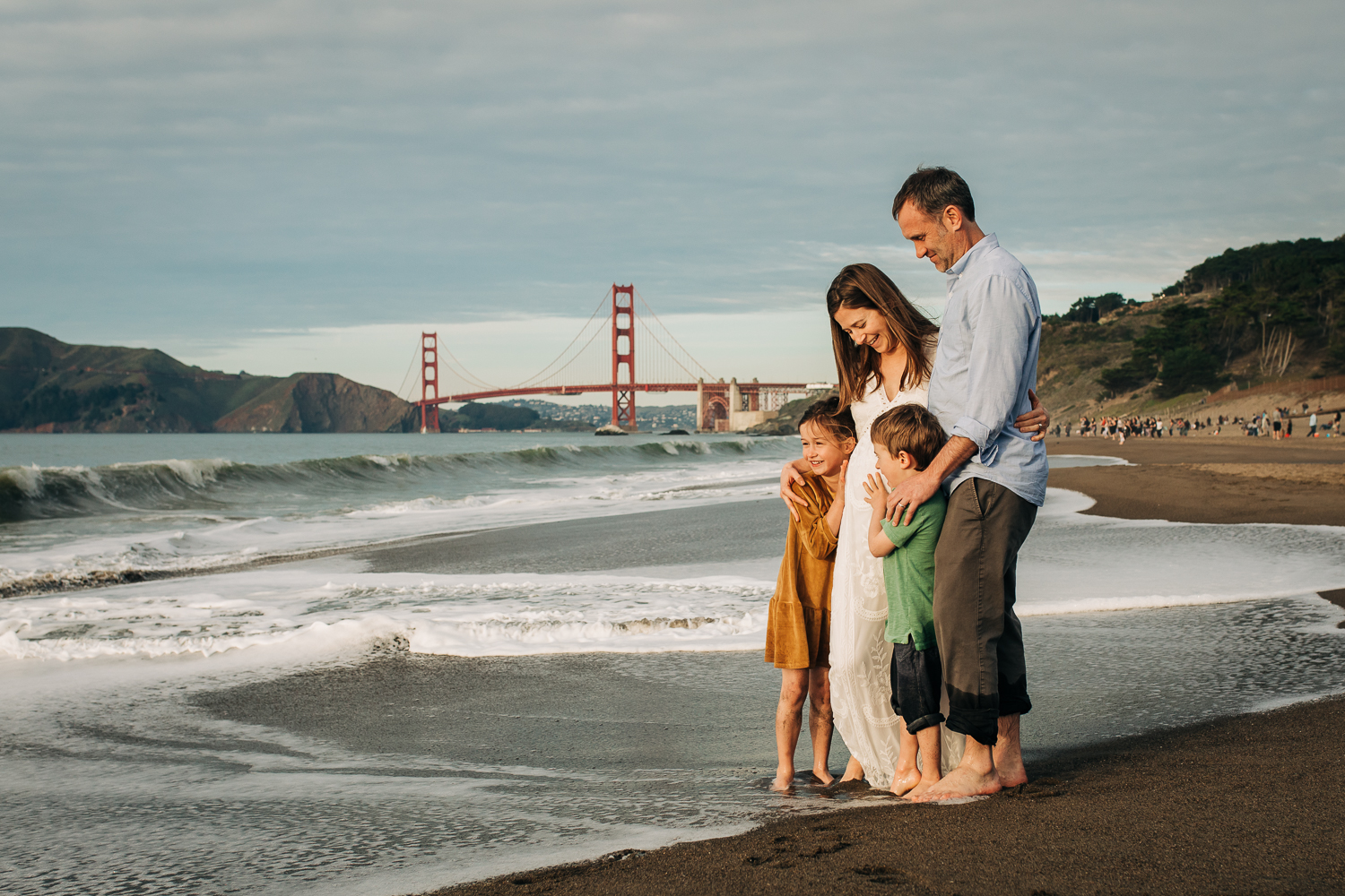 boy and a girl with both parents standing at Baker beach with the San Francisco Golden Gate Bridge in the background 