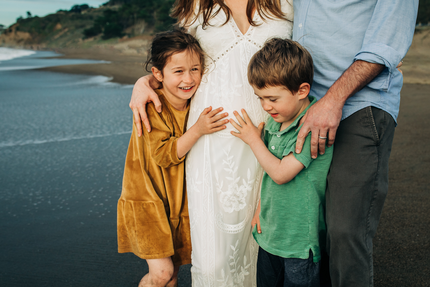 a boy and a girl standing in front of their parents with their hands on their mother's baby bump 