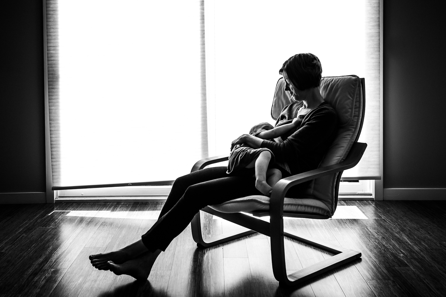 Mother breastfeeding her daughter in front of a window | San Francisco Baby Photographer