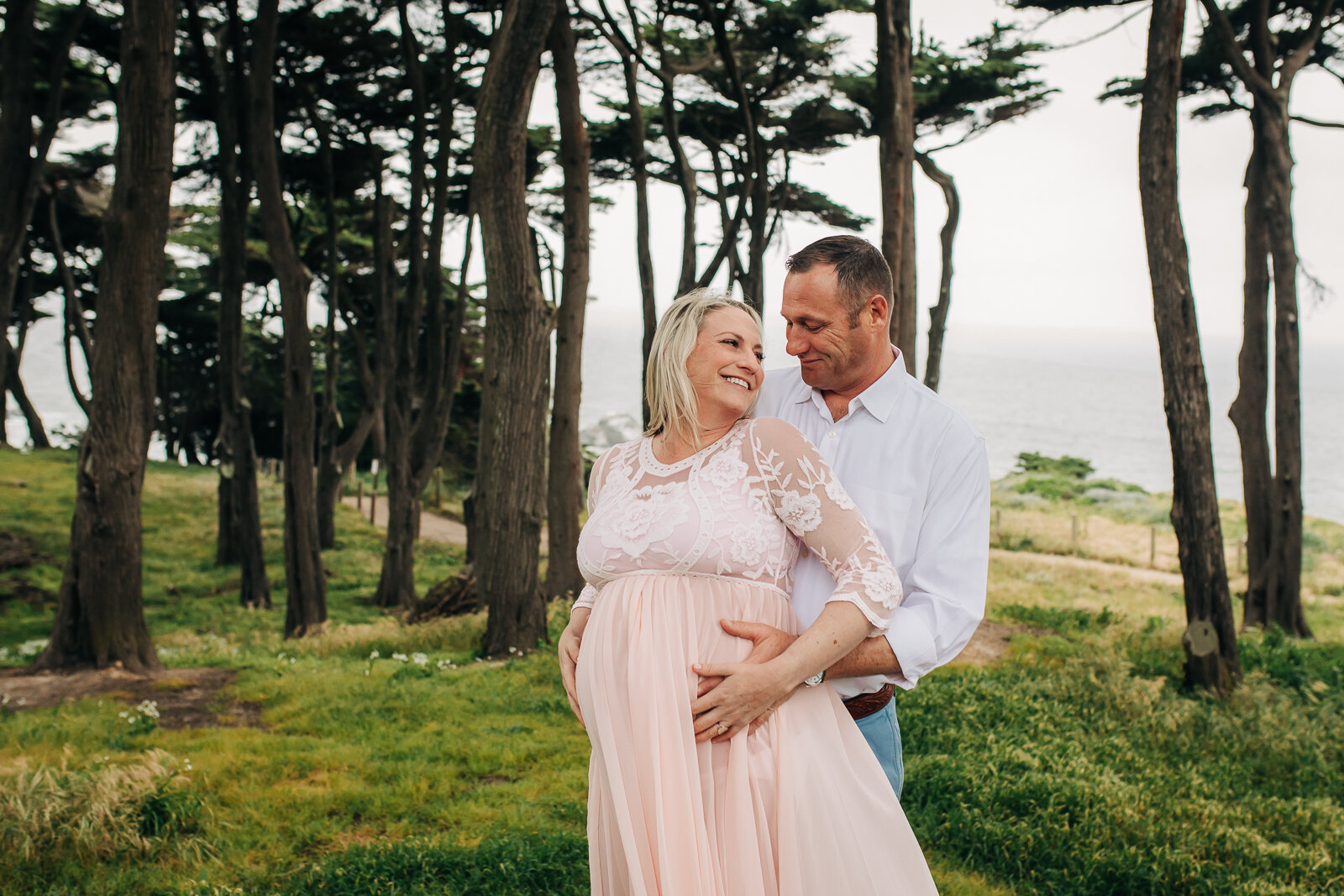 pregnant wife turning towards her husband as he stands behind her and embracing her belly 