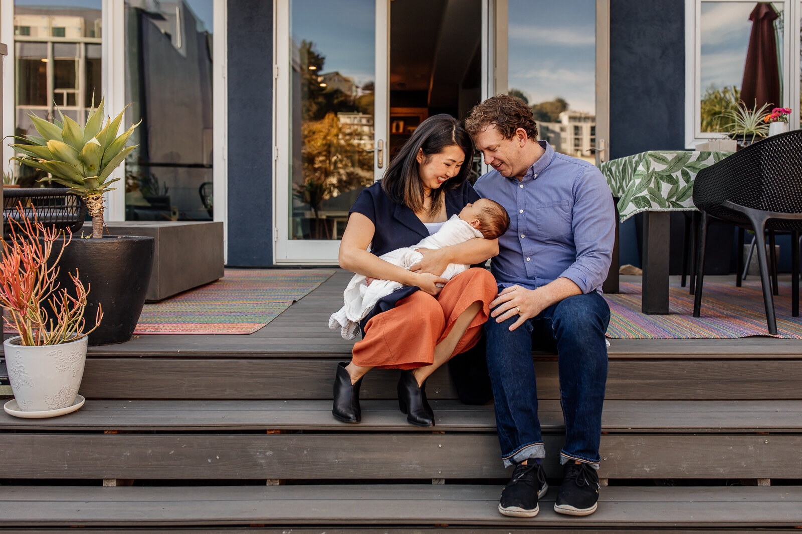 parents sitting on stairs of back deck holding baby boy 