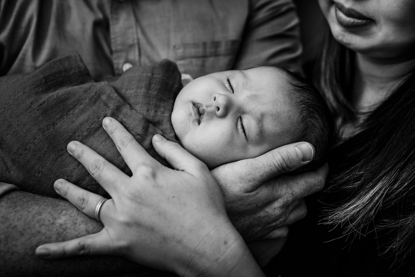 swaddled baby sleeping in mom and dad's arms 