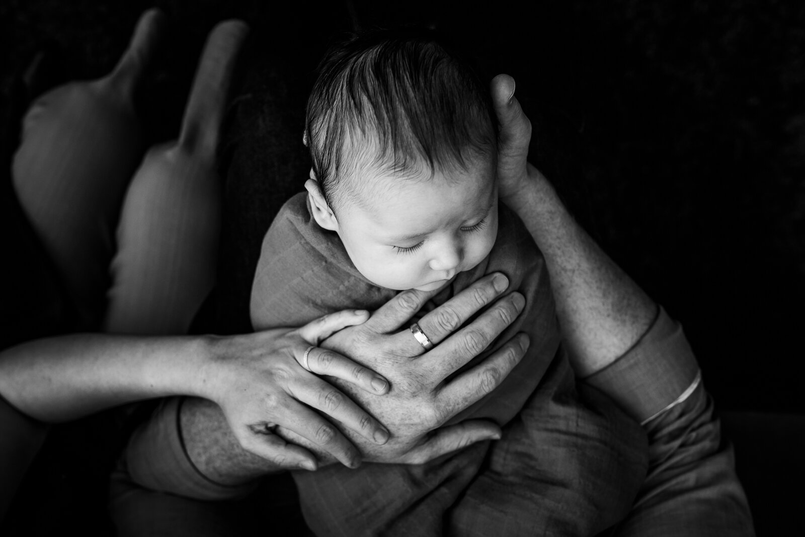 birds-eye view of baby boy in dad's arms with mom's hand touching him 