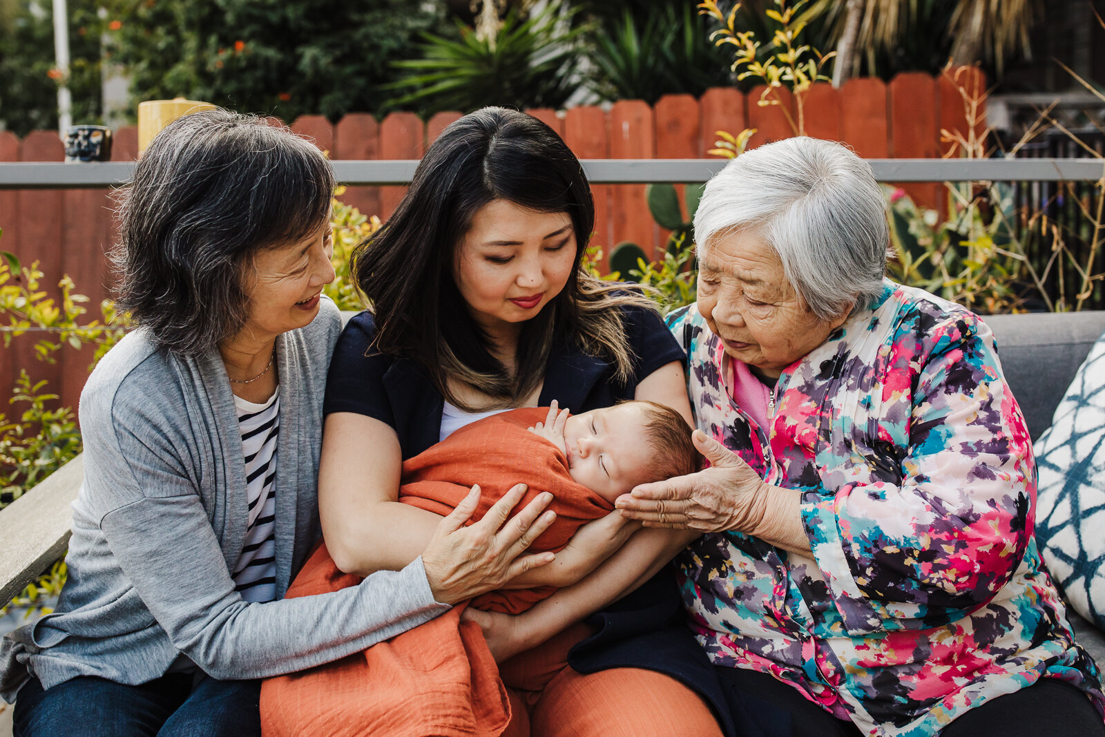 A grandmother, great-grandmother, daughter and grandson all sitting together and looking down at baby boy documenting 4 generations during an Oakland newborn session.