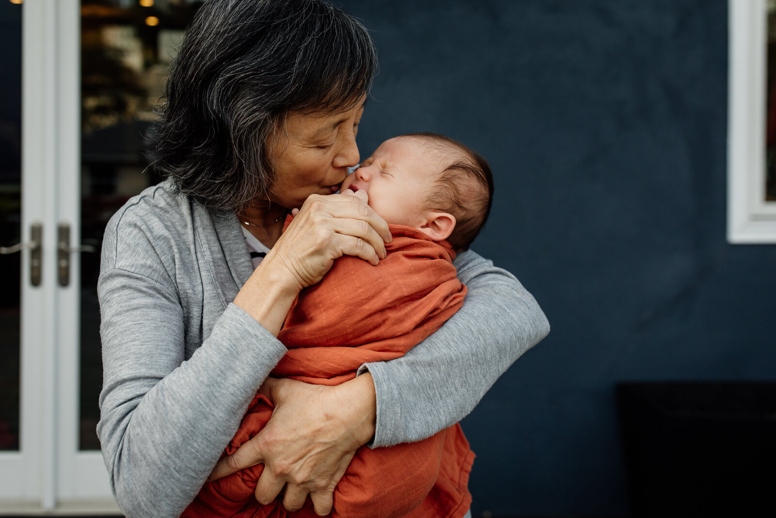 A grandmother holding and comforting baby grandson as he cries during a newborn photo session.