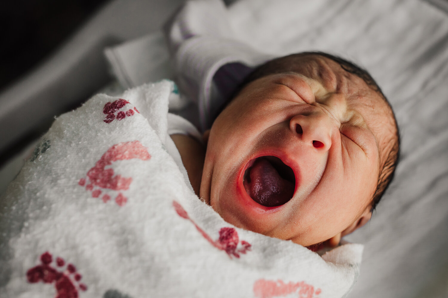 swaddled newborn in hospital bassinet yawning