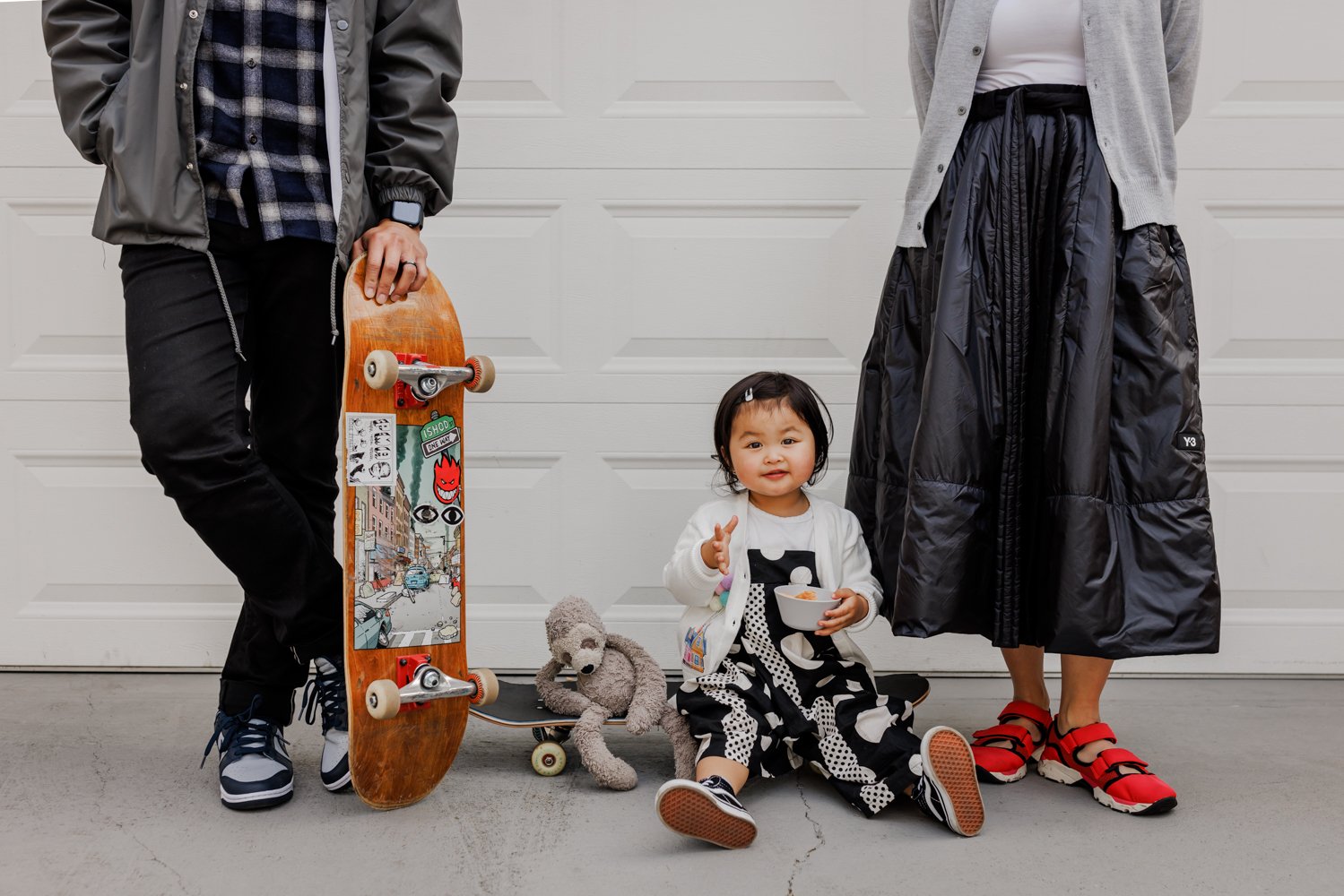 toddler sitting on skateboard between standing parents