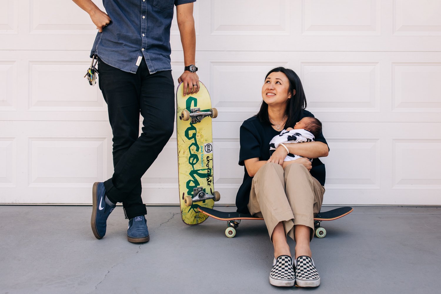 mom holding baby looking up at husband who is holding skateboard