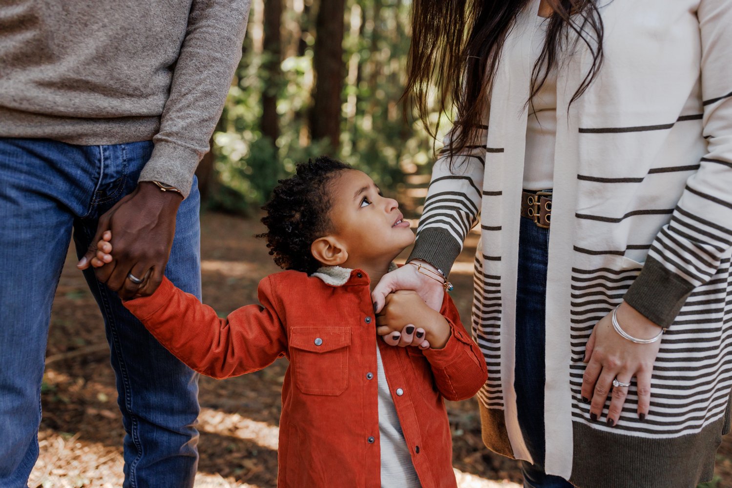 little boy holding parents' hands and looking up at mom